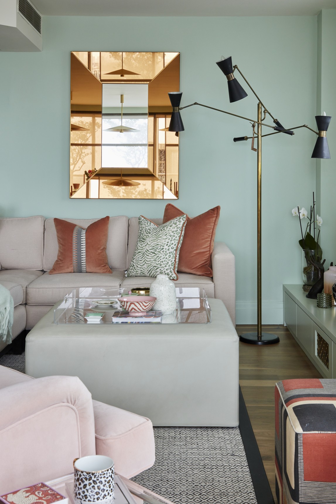 Penthouse lounge with pale green walls, copper-framed mirror, and coral velvet cushions