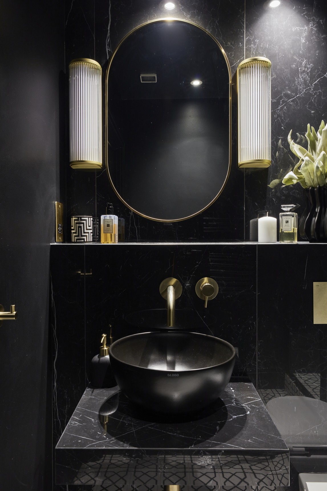 Black stone vanity with gold tap, oval mirror, and wall lighting in London penthouse bathroom