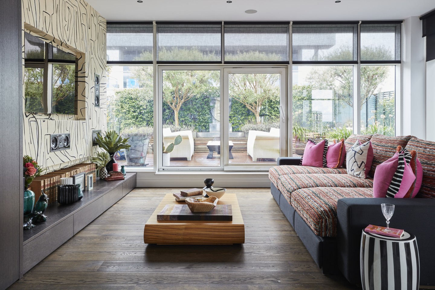 Top floor media and party room in a London penthouse with patterned sofa, pink cushions, and panoramic river terrace views.