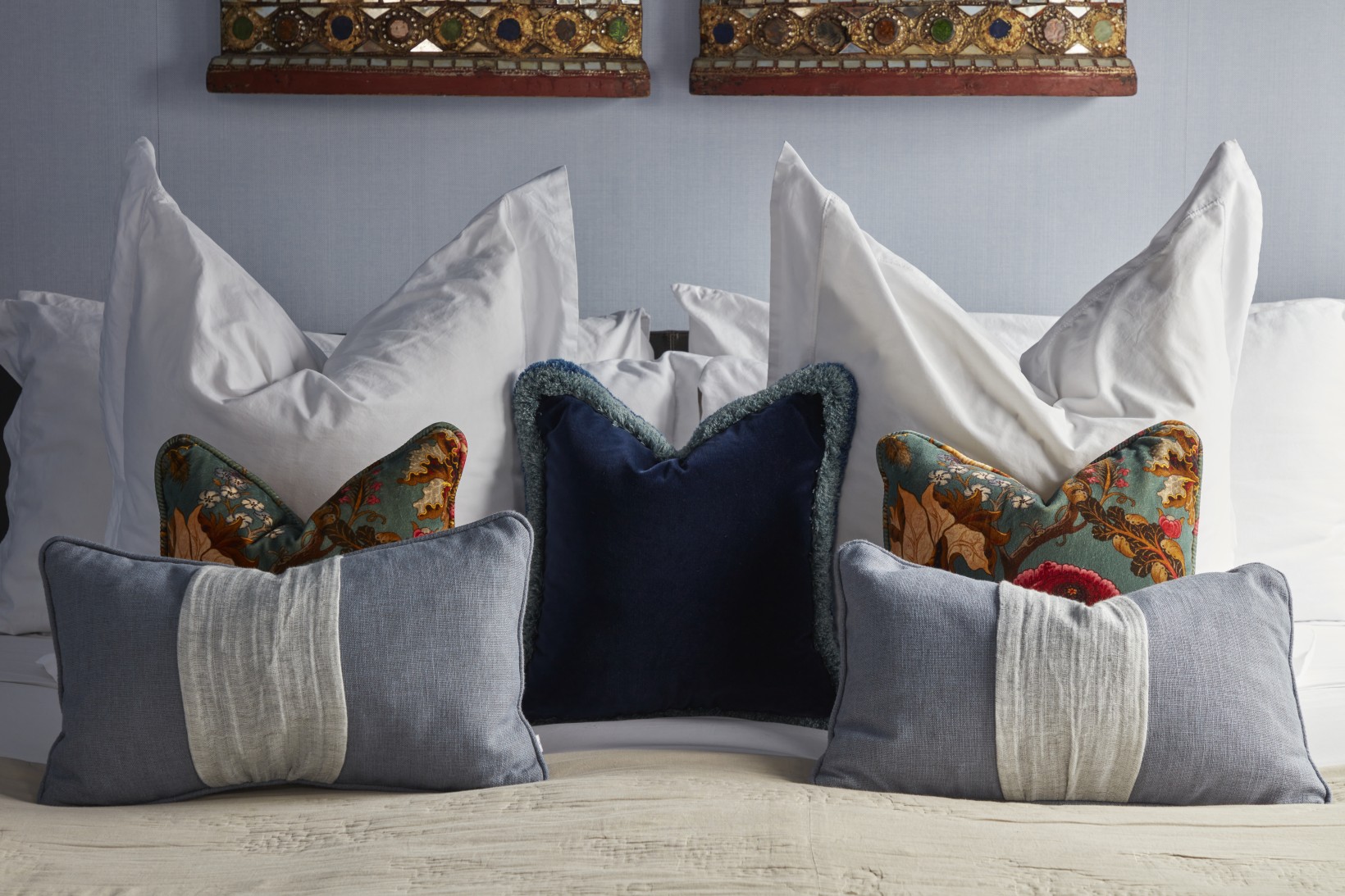 Close-up of guest bedroom in London penthouse featuring layered cushions in navy, soft blue, and heritage floral against crisp white bedding.