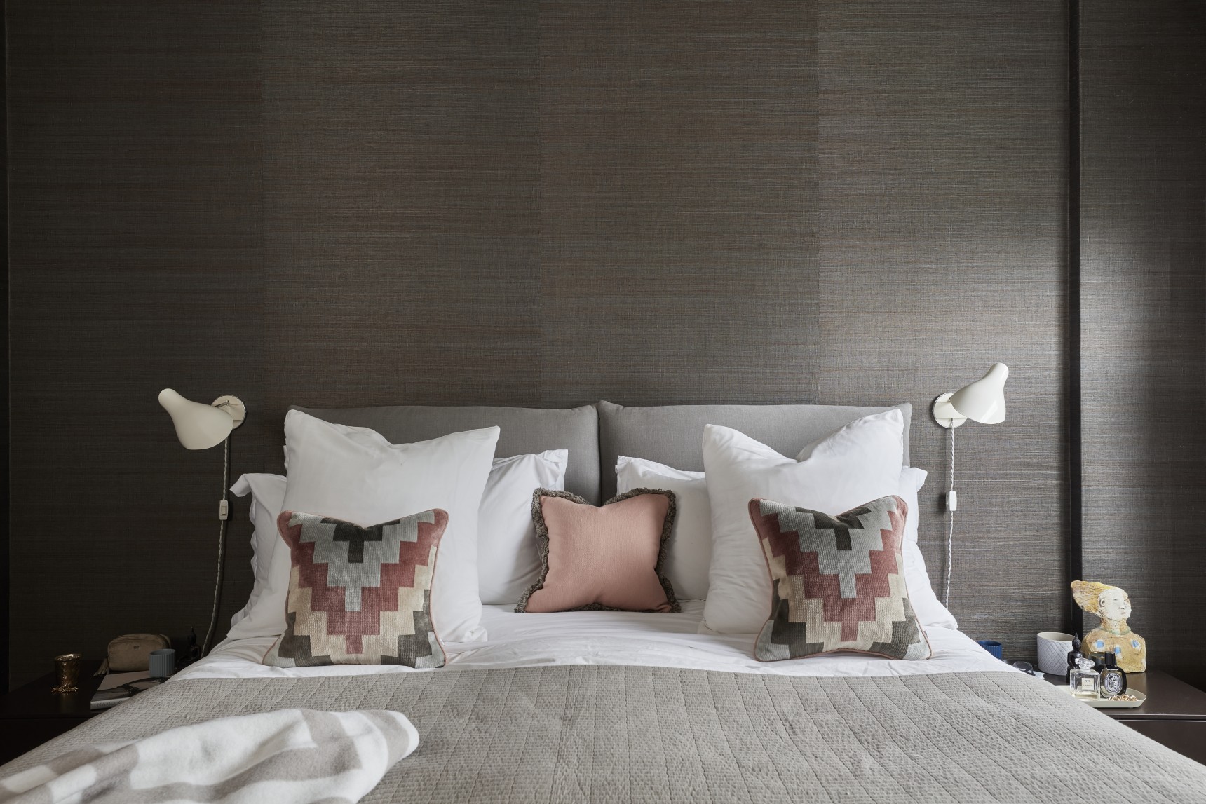 London luxury bedroom with textured wallpaper, bespoke headboard, and layered pillows in warm neutral tones.