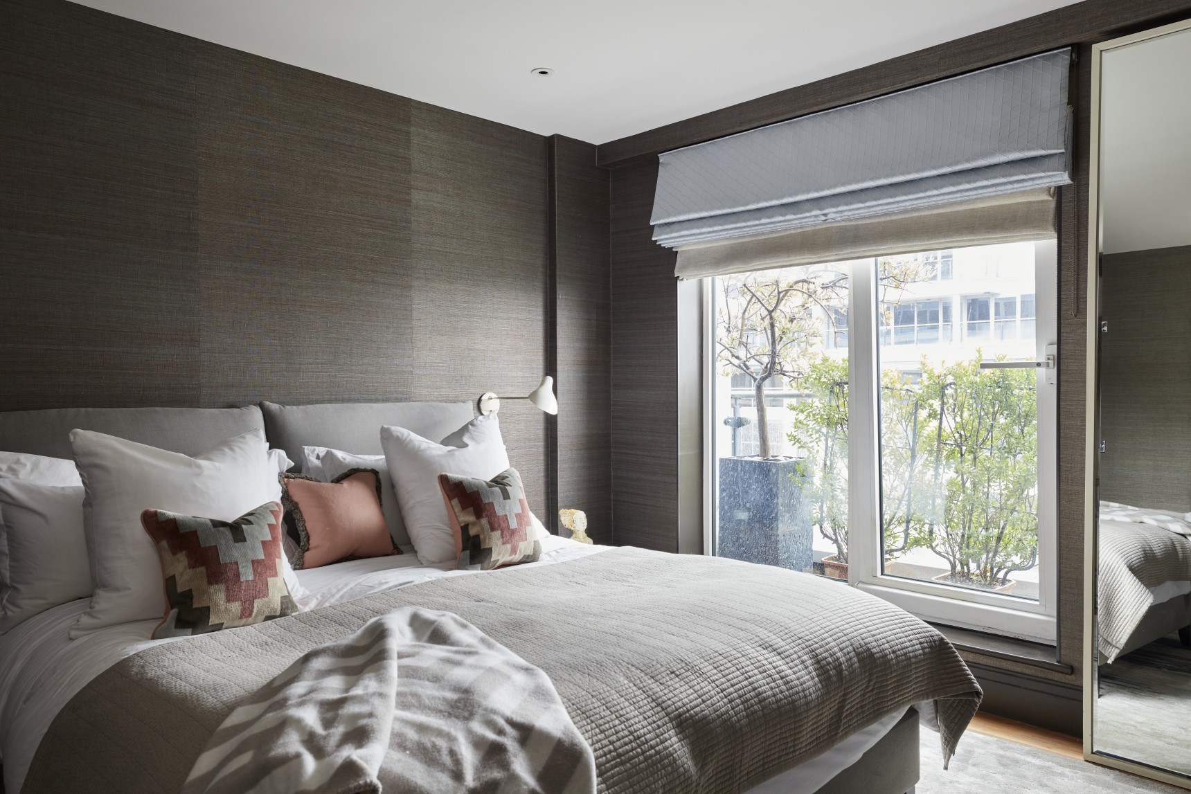 Luxury master bedroom design in London penthouse with chocolate brown textured walls, bespoke upholstered bed, and layered cushions.
