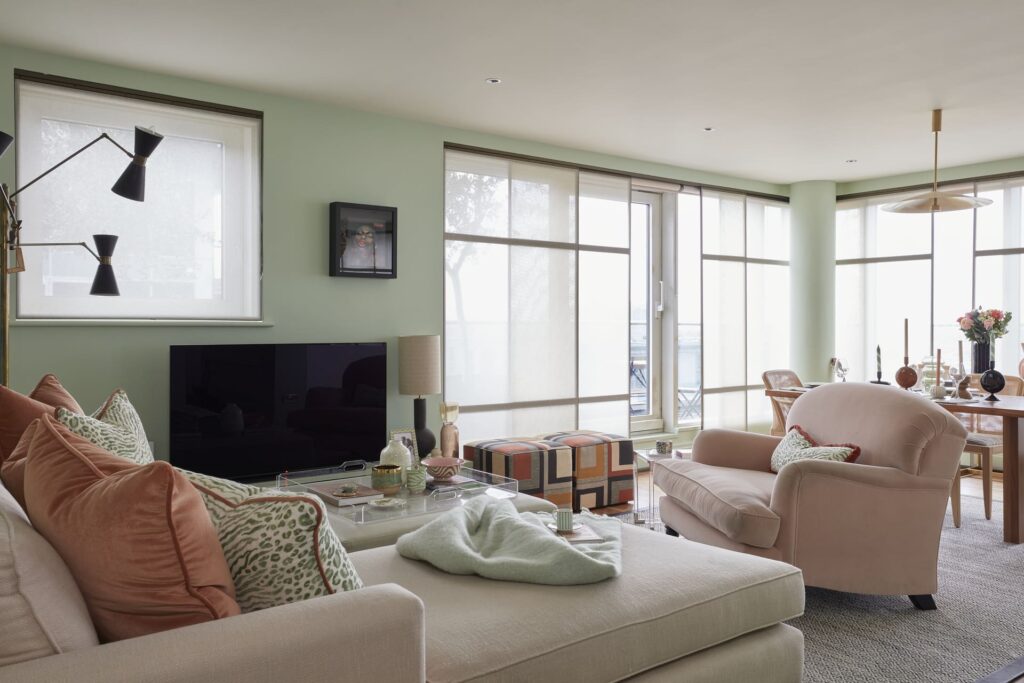 Calming living room with soft green walls, layered textures, and natural light, designed to support wellbeing by Emma Green Design.