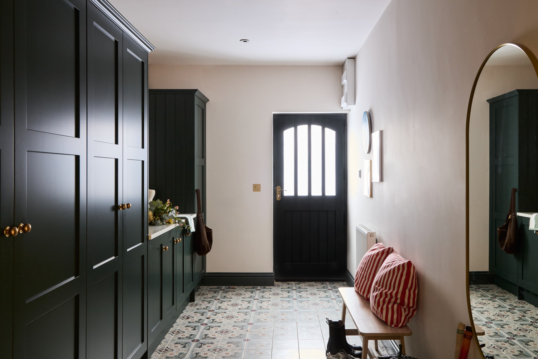 Boot room with green cabinetry patterned tiles bench seating and black door