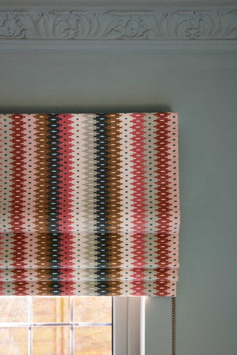 Patterned roman blind and pleated curtains in green living room