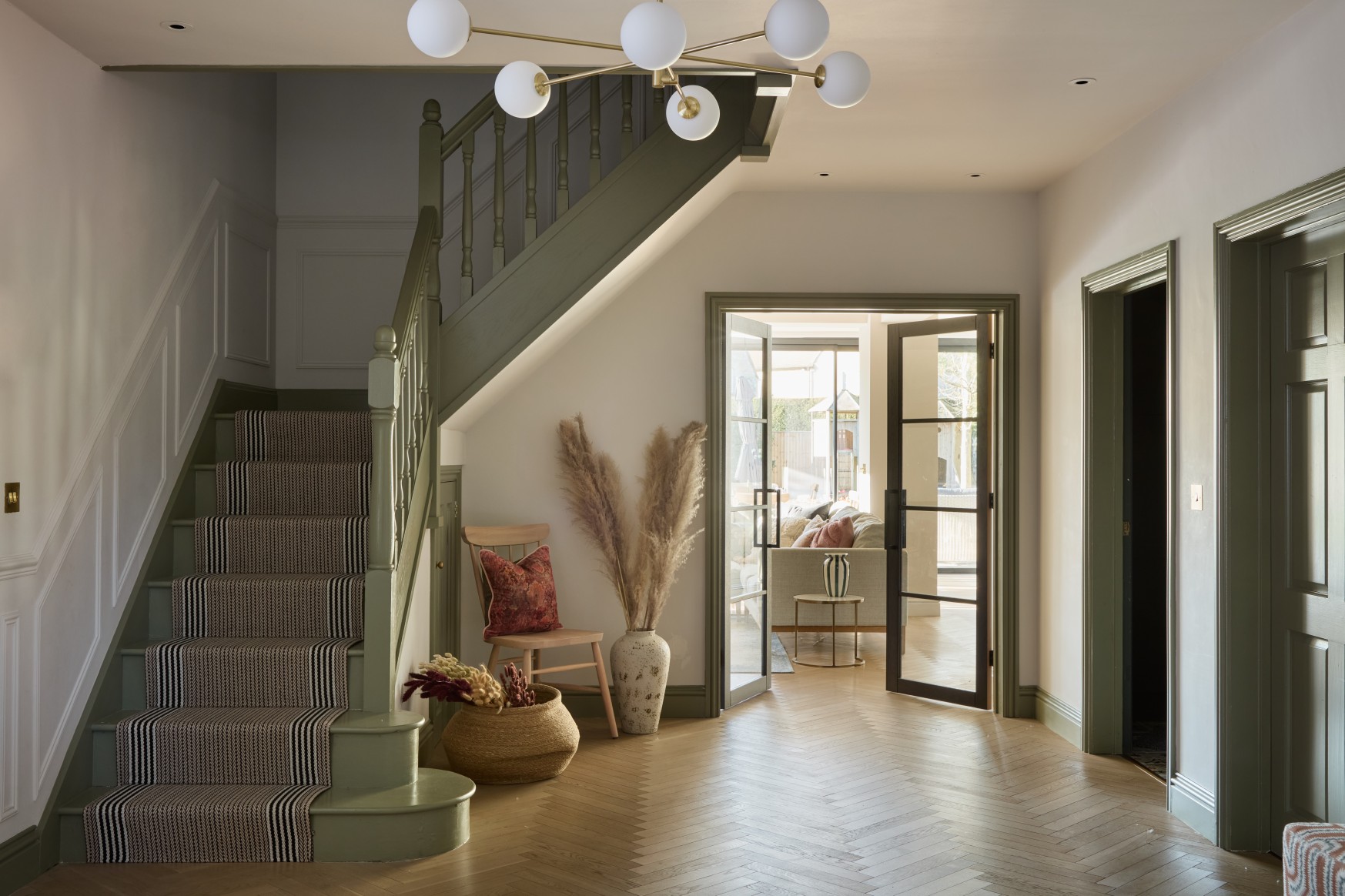 Entrance hall with green staircase herringbone floor and glazed doors to living room