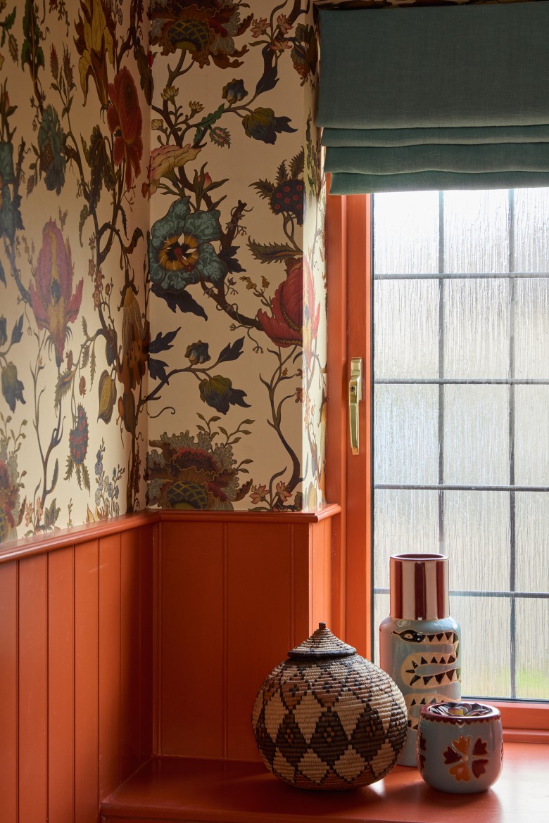 Cloakroom window detail with terracotta joinery, Roman blind, decorative ceramics, and botanical wallpaper