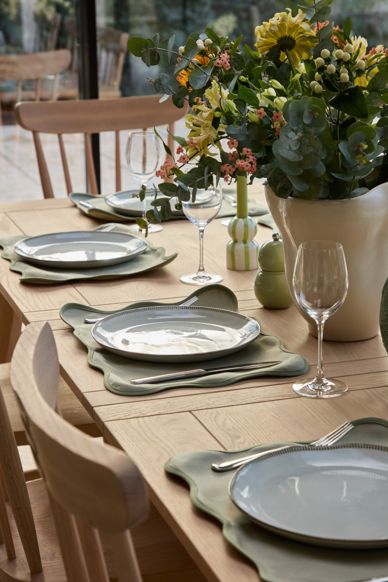Dining table with green tableware and flowers in open plan kitchen